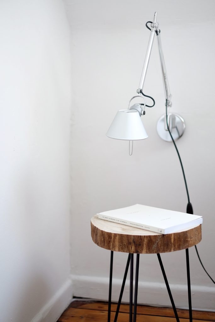 Une jolie table de chevet fait avec un rondin de bois et des pieds métalliques noirs en forme d'épingle.
